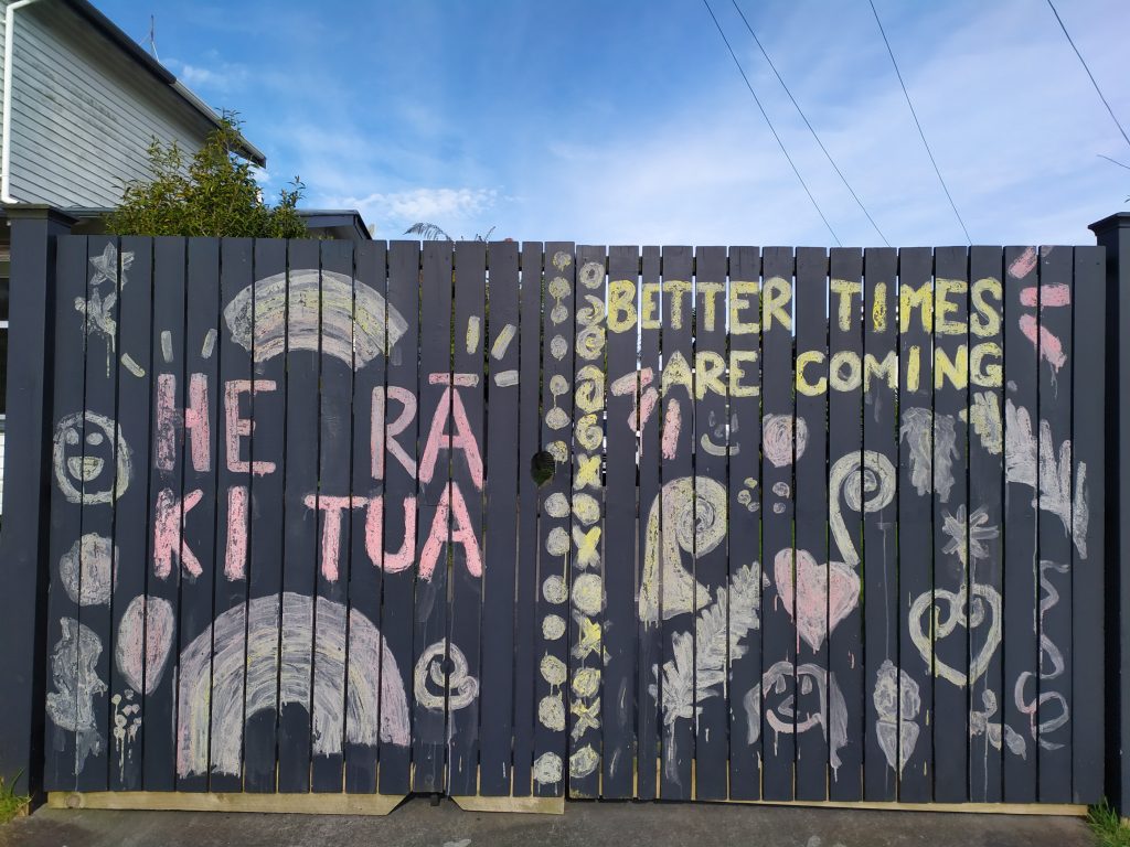 Artwork on a fence reading: He ra ki tua (better times are coming)