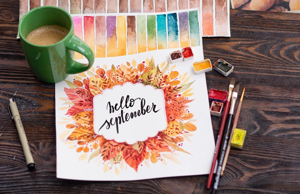 Painted page saying "hello September" surrounded by paints and brushes