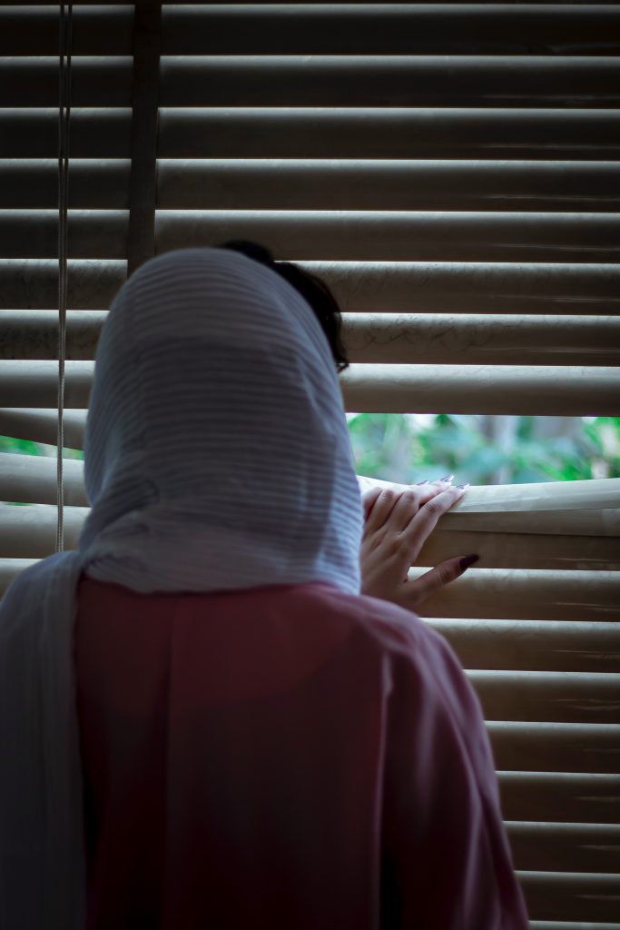 Woman peeking out the window through the blinds. 