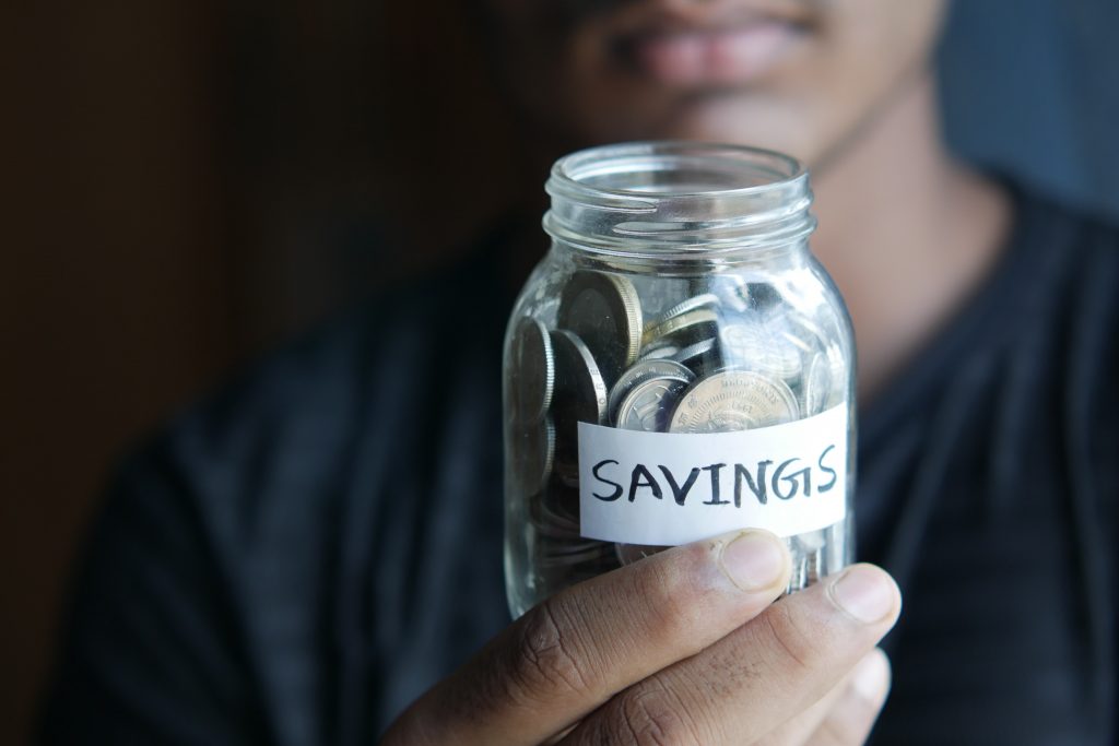 Person holding a jar filled with coins marked "savings"